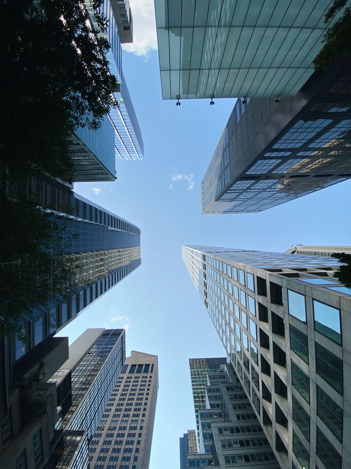 Low-angle view of modern skyscrapers converging towards the sky under a bright blue sky.